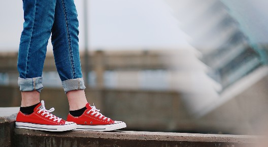 person wearing red converse walking on narrow wall
