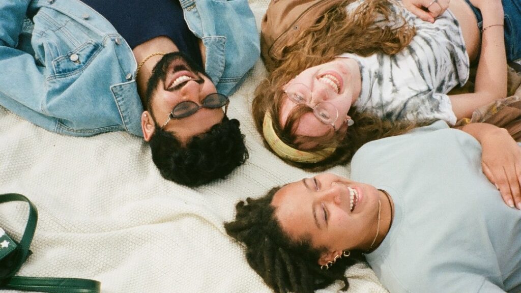 image of three young people laying on a blanket looking up and smiling